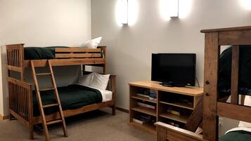 Una cama litera con escalera, un televisor sobre un soporte de madera y una estantería con libros.