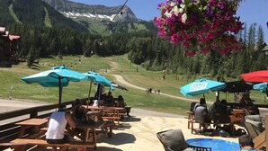 Un espace extérieur aménagé avec des tables et des chaises en bois, une piscine et une vue sur une chaîne de montagnes.