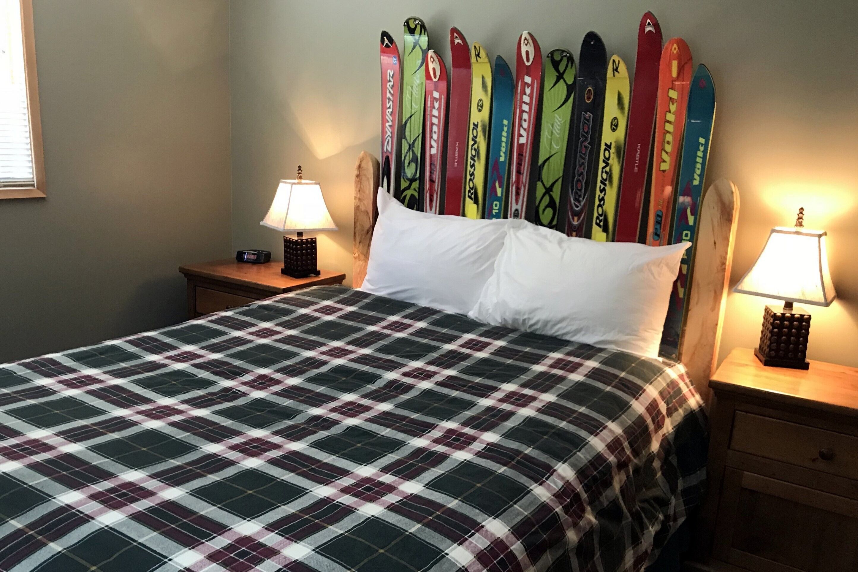 Una cama con colcha escocesa, dos mesitas de noche con lámparas y una pared decorada con esquíes.
