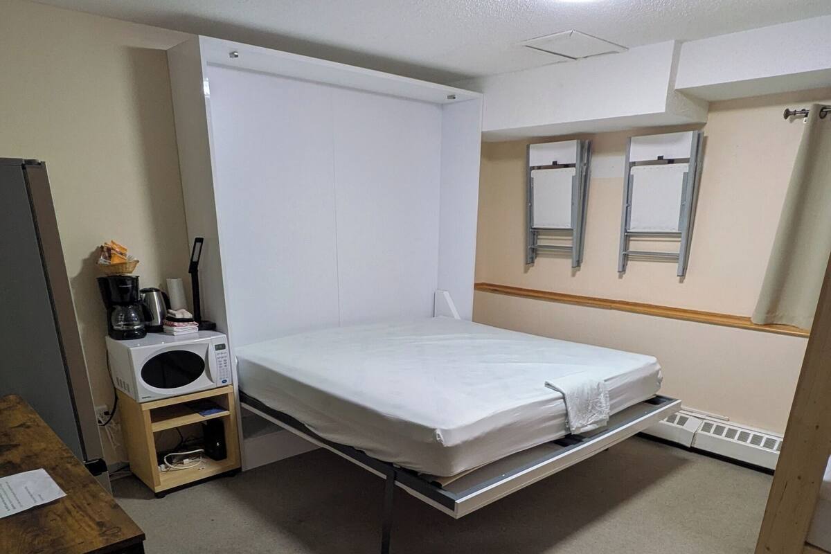 Une petite pièce, peu meublée, avec un lit simple, une petite table, un four à micro-ondes et un radiateur.