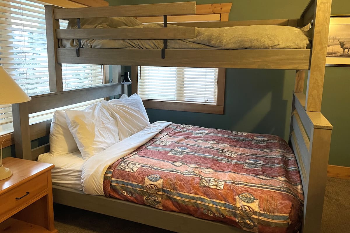 A bunk bed with a patterned bedspread, a bedside table, and a lamp.