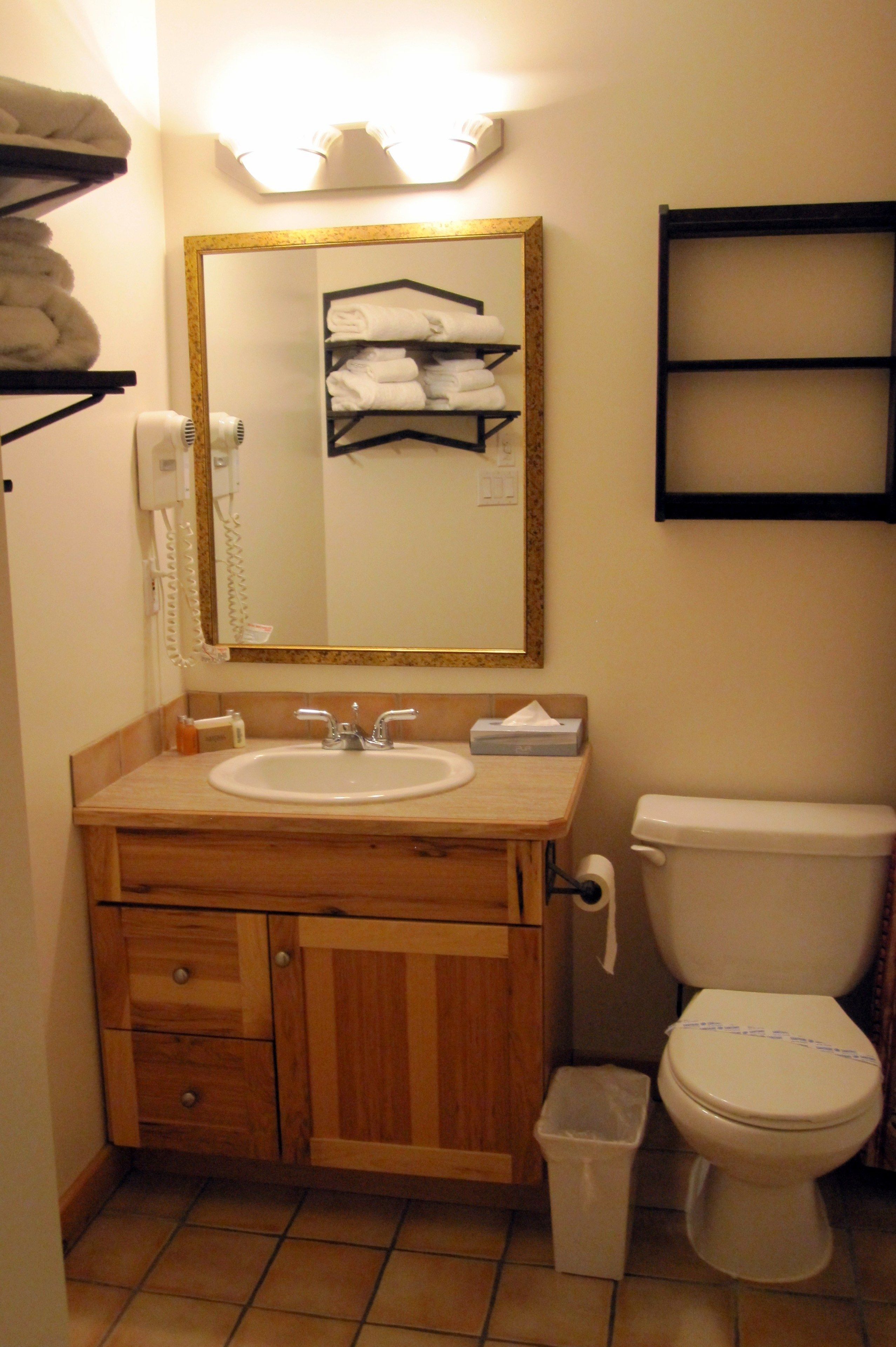 Une salle de bain avec un meuble-lavabo en bois, un évier, un miroir, des toilettes et une poubelle.