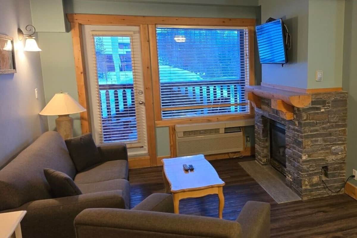 A cozy living room with a stone fireplace, a sofa, a coffee table, and a television mounted above the fireplace.