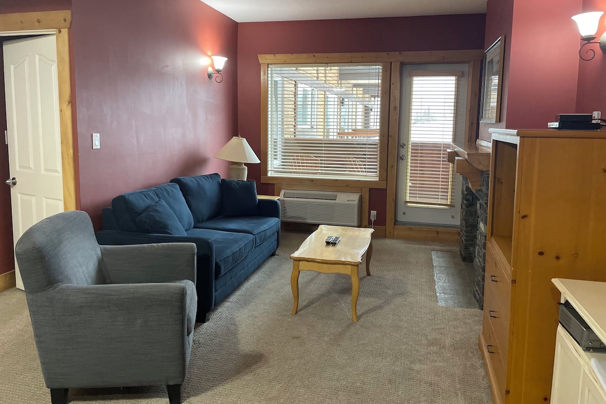 A living room with a blue sofa, a grey armchair, a wooden coffee table, and a wooden cabinet.