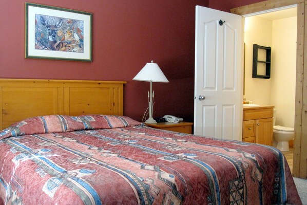 Une chambre à coucher avec un lit, une table de chevet, une lampe, une porte et un tableau encadré au mur.