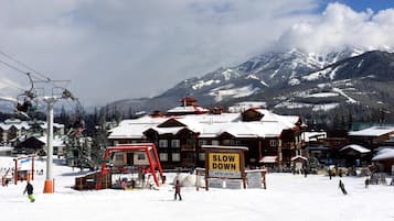 Ein Skigebiet mit einem 'SLOW DOWN'-Schild, Skipisten und schneebedeckten Bergen im Hintergrund.
