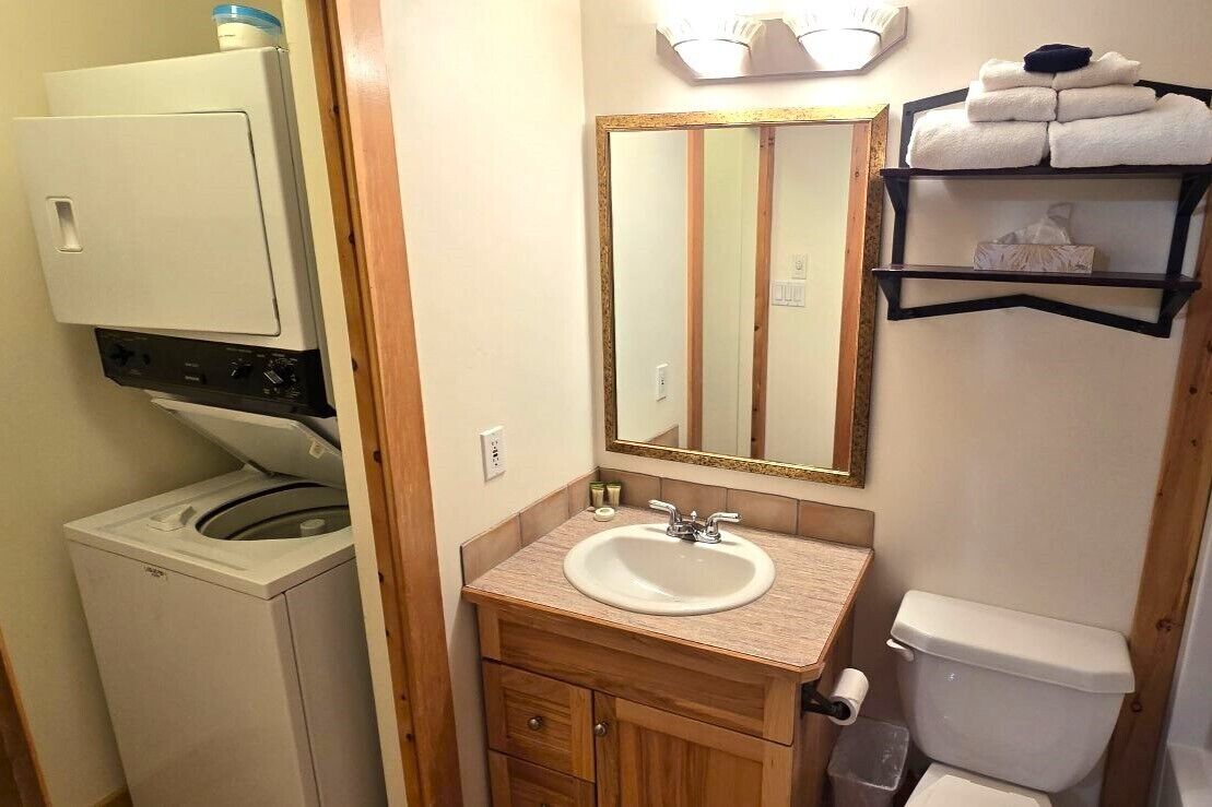 A compact bathroom with a washing machine, a sink, a mirror, and a towel rack.