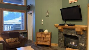 A cozy living room with a fireplace, a television mounted above it, and a comfortable seating area with a sofa and a chair.
