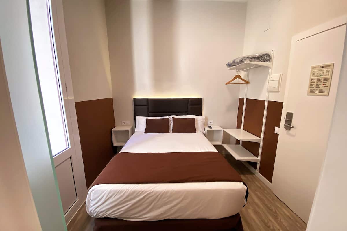 A hotel room with a large bed, bedside tables, a wardrobe, and a window.