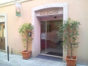 Exterior del Hotel Bonavista, con una entrada despejada, un código QR en la puerta de vidrio y dos macetas a cada lado.