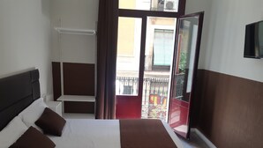 Een hotelkamer met een bed, een bureau en een raam met uitzicht op het balkon.