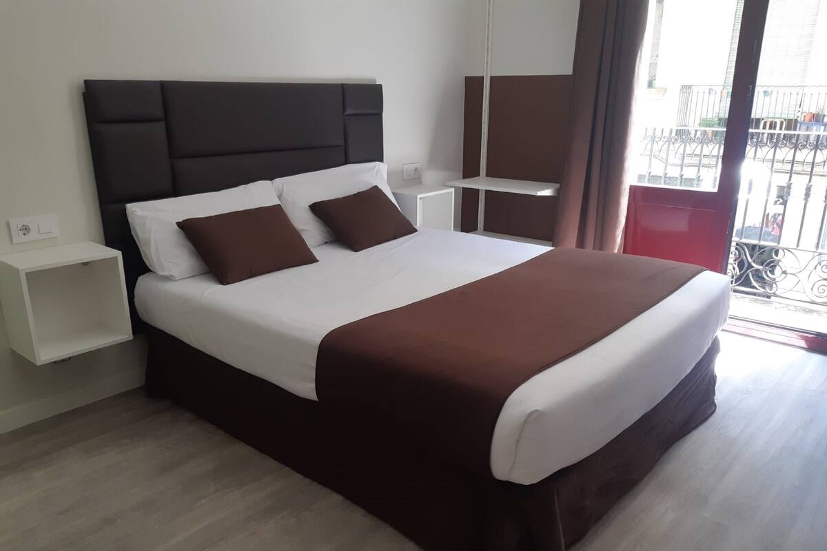 A modern hotel room with a large bed, a bedside table, a nightstand, and a view of the outside balcony.