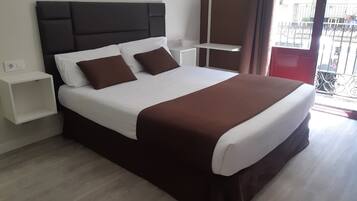 Una habitación de hotel moderna con una cama grande, una mesita de noche y vistas al balcón exterior.