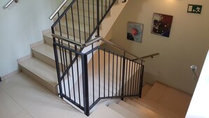 Een trap met een metalen leuning, een wandlamp en een bord met daarop een nooduitgang.