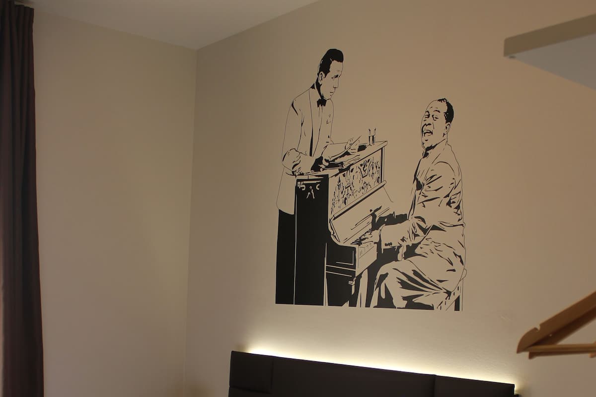 A hotel room with a large bed, a headboard, a nightstand, and a wall-mounted artwork.