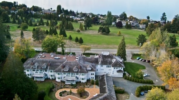 A large, white, multi-story building with a symmetrical facade, surrounded by a well-maintained lawn and trees. - Crown Mansion Boutique Hotel & Villas (Qualicum Beach)
