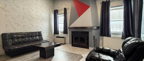 Una sala de estar moderna con un sofá de cuero negro, una mesa de centro y una chimenea.