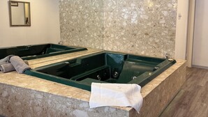 Une salle de bain avec deux grandes baignoires rectangulaires de couleur verte, des murs en marbre et un plan de toilette en marbre.