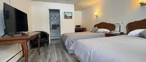 A hotel room with two beds, a desk with a TV, a chair, a door, and a small table with a lamp.