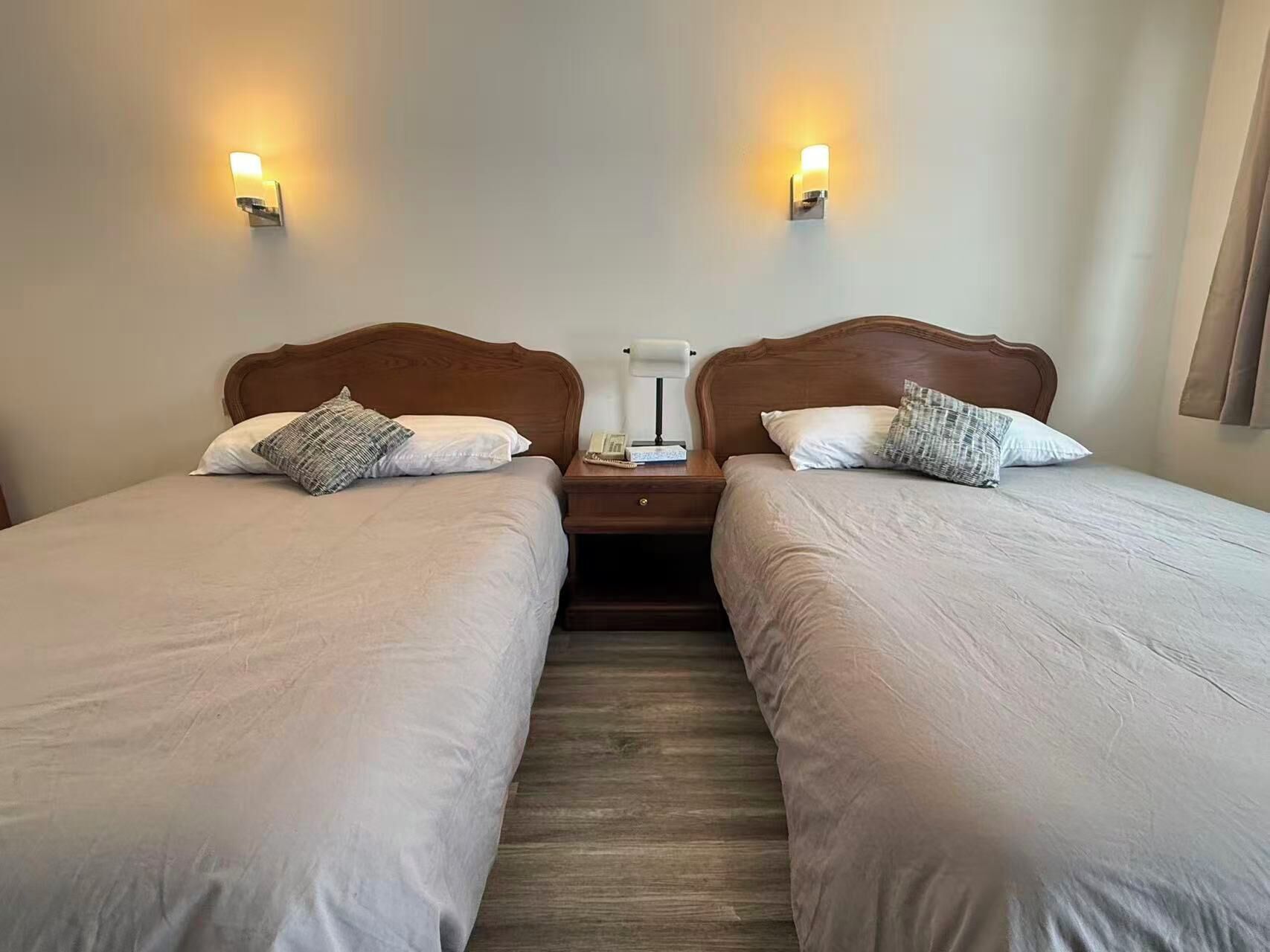 Habitación doble con dos camas, cada una con cabecero de madera y ropa de cama blanca. Hay dos lámparas de pared a cada lado de las camas.