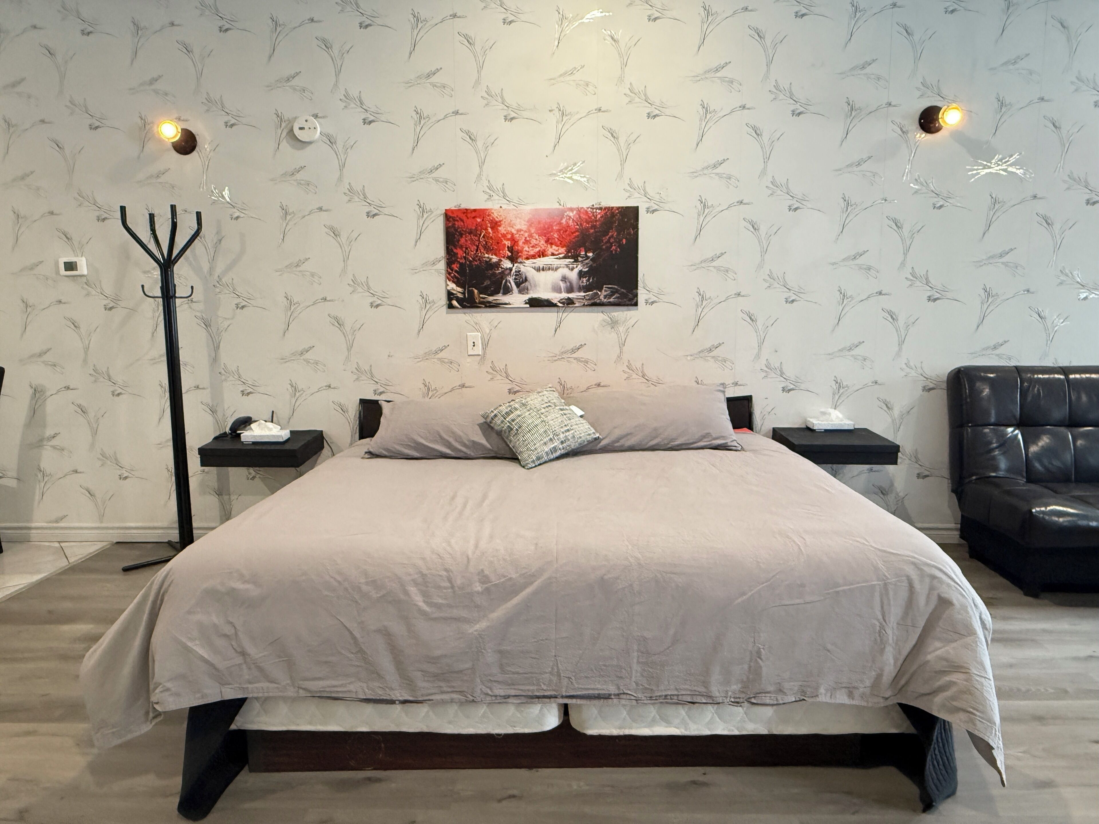 A bedroom with a bed, a nightstand, a lamp, a couch, and a wall-mounted picture.