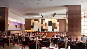 A modern restaurant with a central bar area, multiple dining tables, and a patterned wall design. - Ramee Rose Hotel (Dubai)