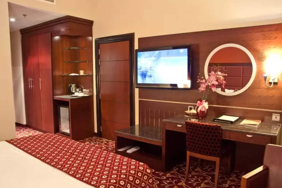A hotel room with a bed, a desk with a chair, a television, a mirror, and a wardrobe.