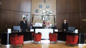 A reception area with two receptionists, a reception desk, and a wall with clocks and a decorative plant. - Ramee Rose Hotel (Dubai)