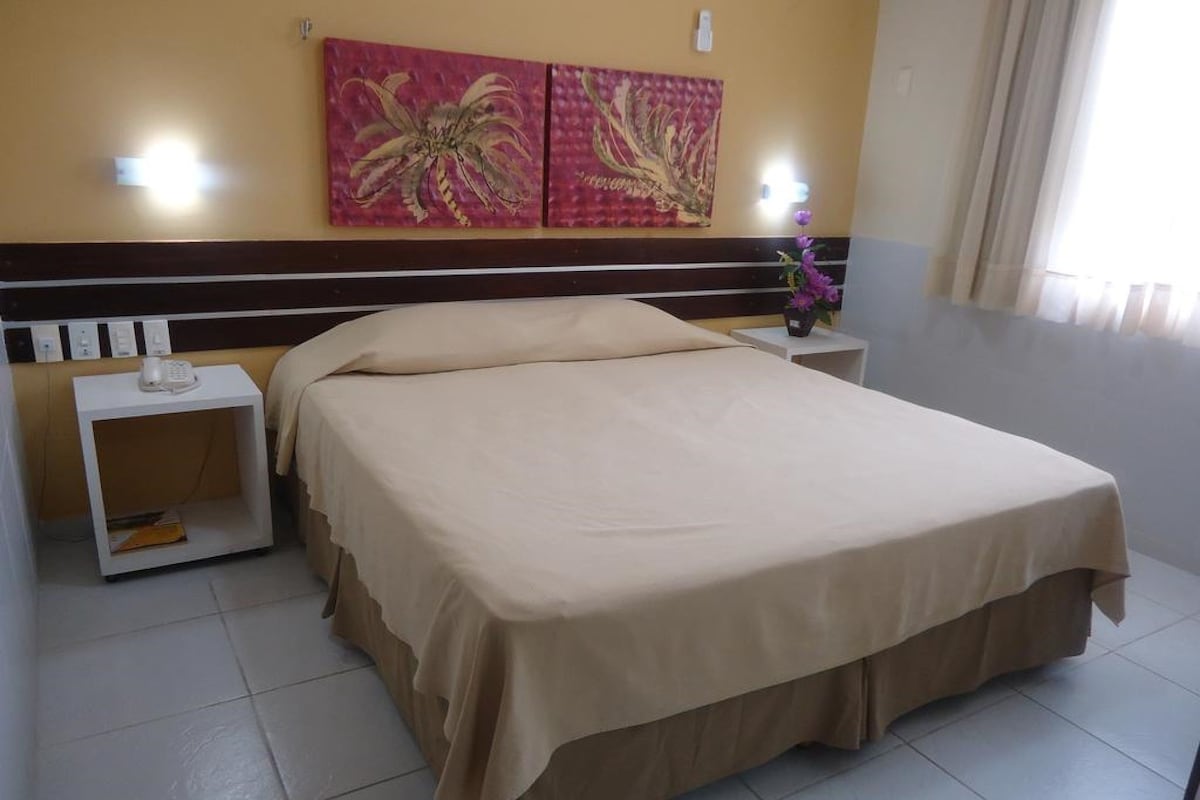 Une chambre d’hôtel avec un lit, une table de chevet, un téléphone et un mur orné de deux tableaux.