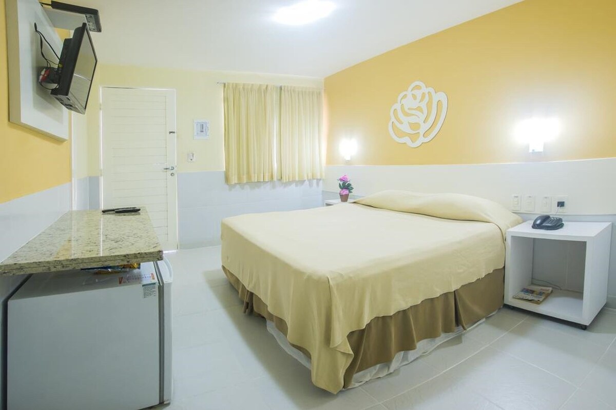 Une chambre d’hôtel équipée d’un lit, d’un bureau, d’une chaise, d’une table de chevet, d’un téléphone et d’un téléviseur fixé au mur.