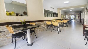 Een ruime, overdekte eetruimte met meerdere tafels en stoelen, een accentmuur van steen en grote spiegels aan de wanden.
