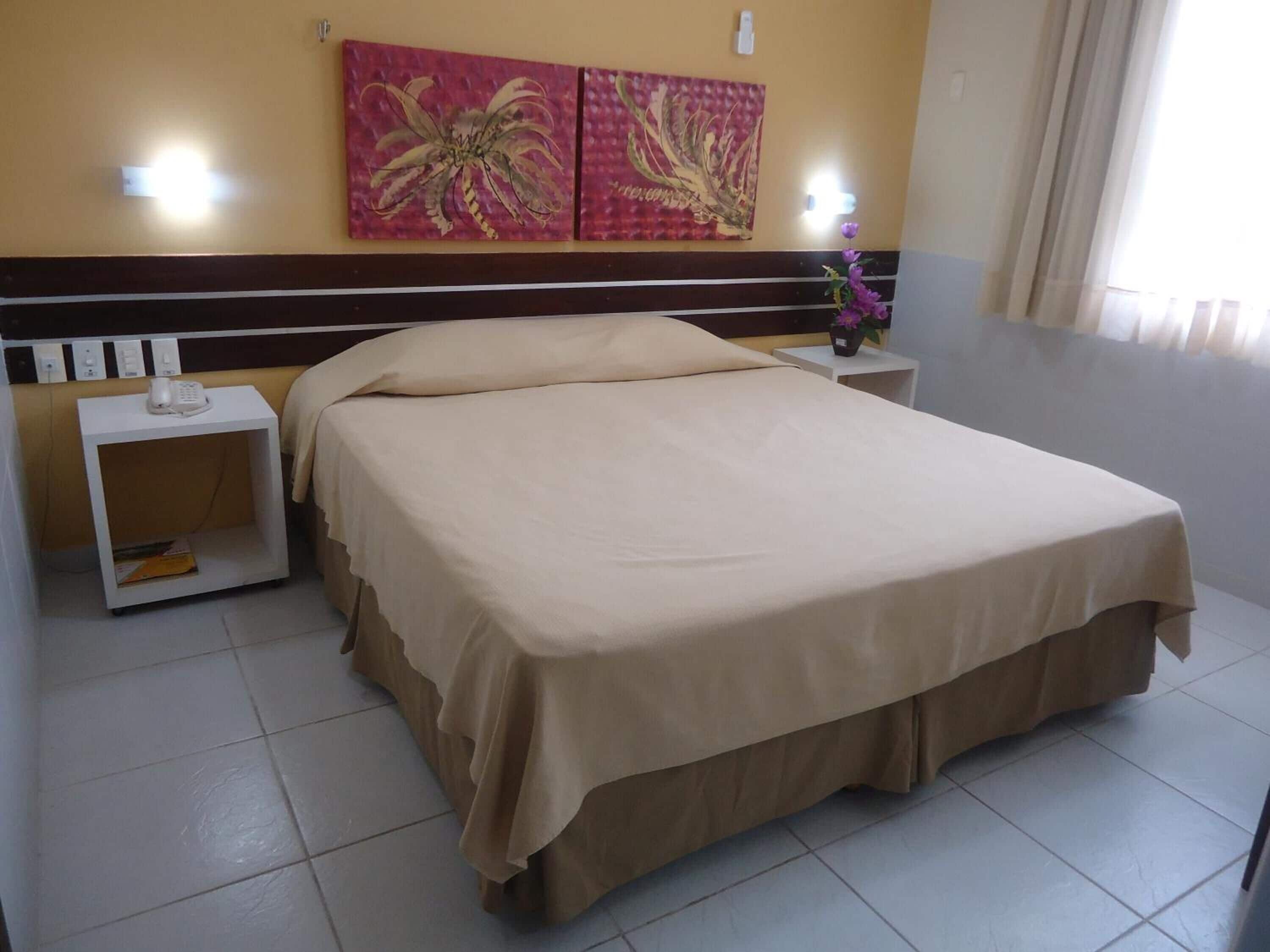 A hotel room with a large bed, a nightstand with a phone, and a wall with two paintings.