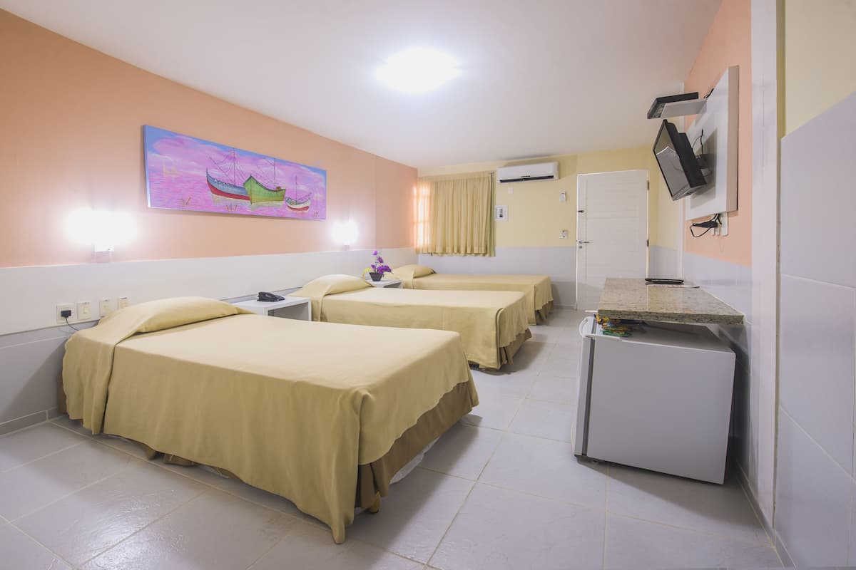 Une chambre d’hôtel avec trois lits, un petit bureau, une télévision et un appareil de climatisation.