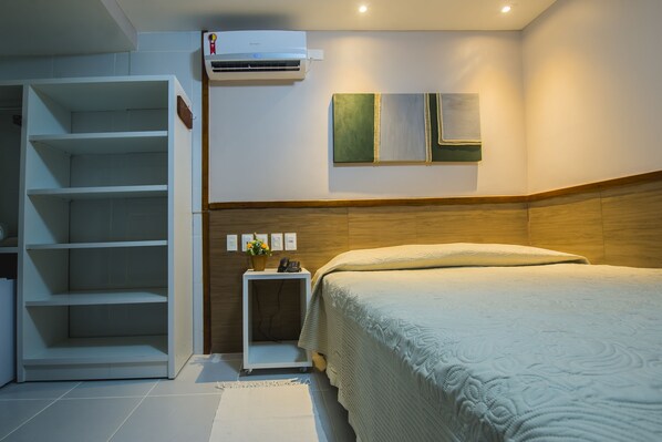 A bedroom with a bed, a white wardrobe, a small bedside table with a lamp, and an air conditioner on the wall.
