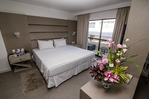 Ein modernes Hotelzimmer mit einem großen Bett, einem Nachttisch, einer Lampe, einer Blumenvase und Blick auf den Balkon.