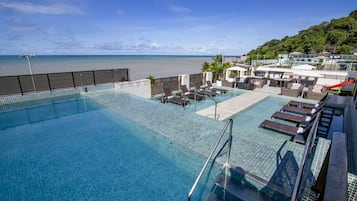 A rooftop infinity pool with lounge chairs and a view of the beach.