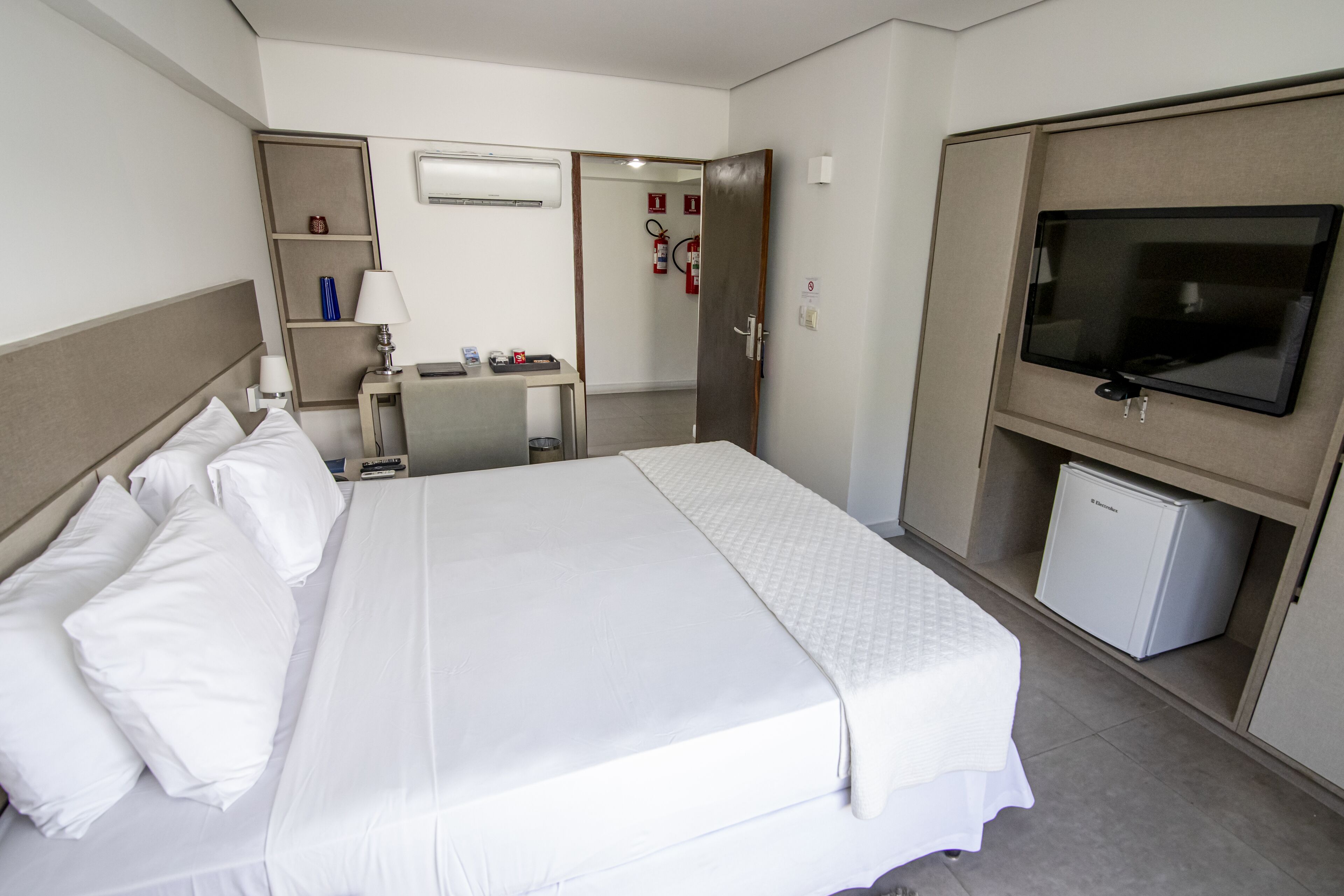 A hotel room with a bed, a desk, a television, and a mini-fridge.
