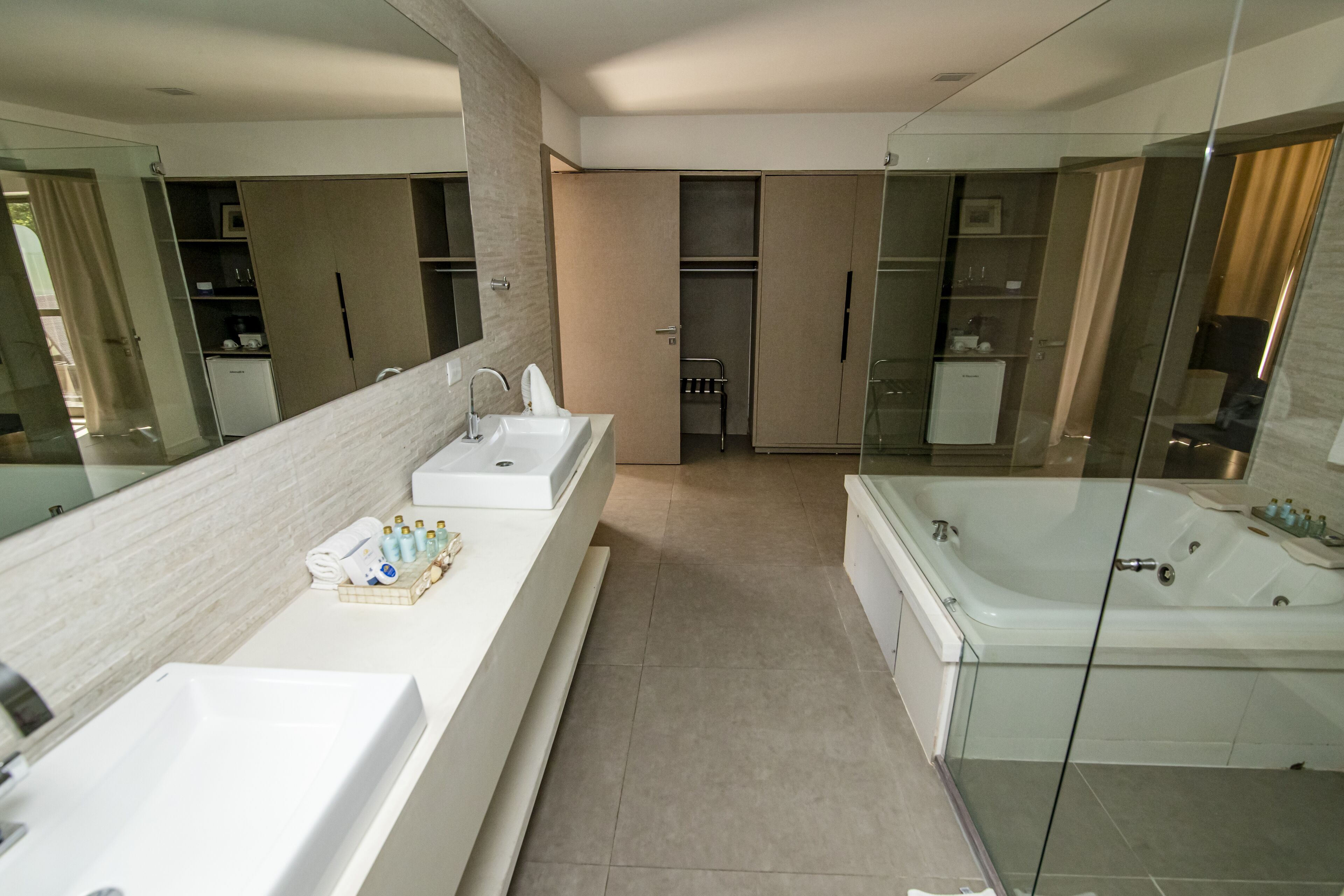 A modern bathroom with a large mirror, two sinks, a bathtub, and a walk-in shower.