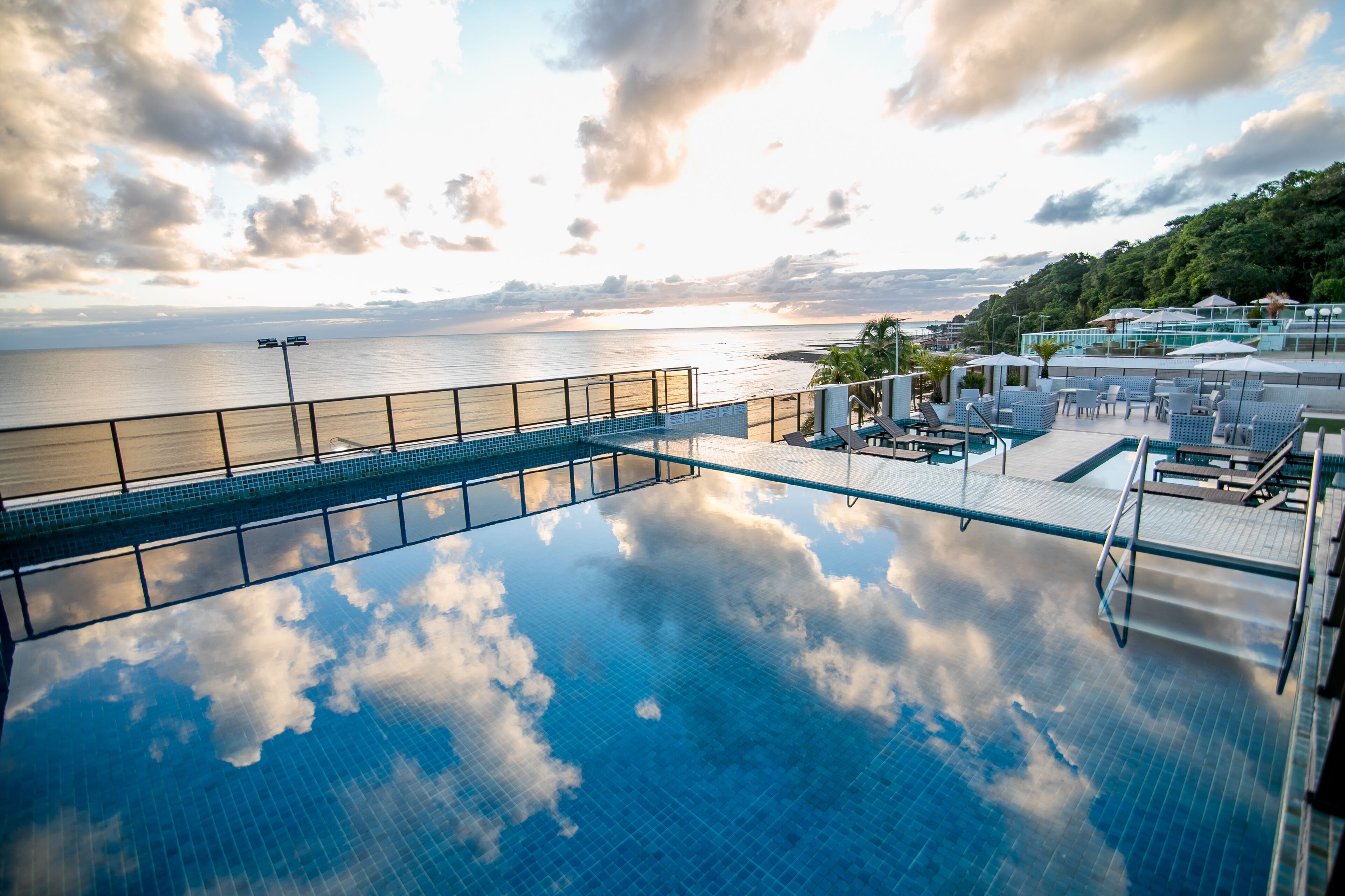 A rooftop infinity pool with a view of the sea and a sunset.