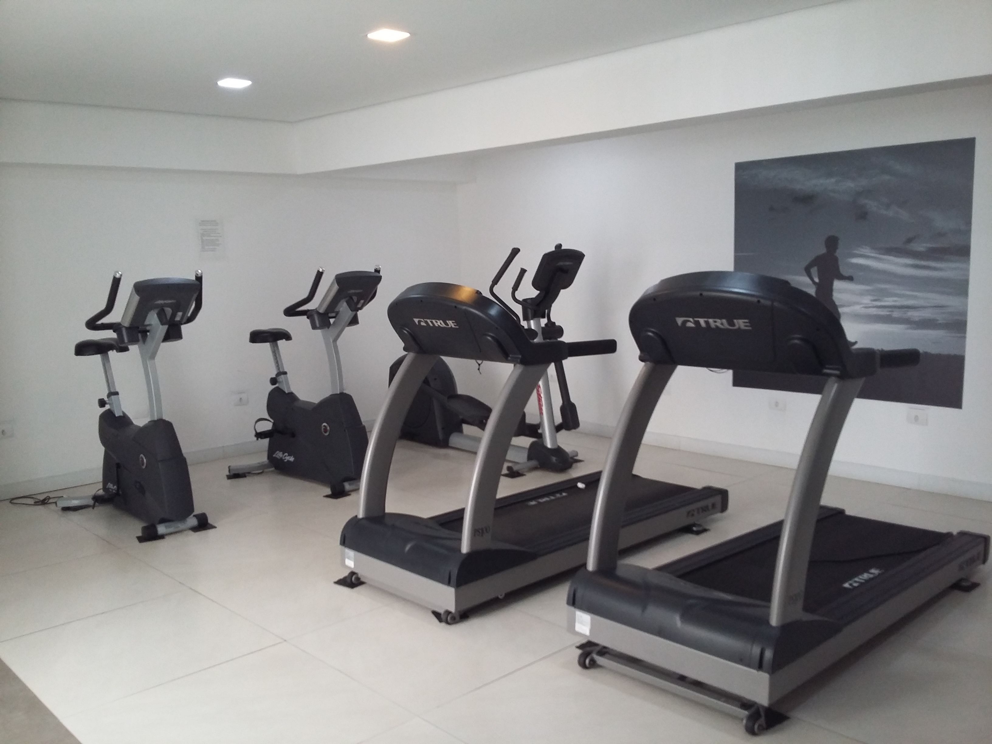 Un gimnasio con tres cintas de correr, una elíptica y una bicicleta estática.