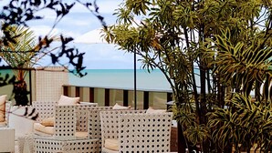 A terrace with wicker furniture, a large potted plant, and a view of the sea. - Hotel Cabo Branco Atlântico (João Pessoa)