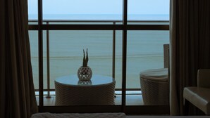 A bedroom with a large window overlooking a body of water, a bed, a round table, and a chair. - Hotel Cabo Branco Atlântico (João Pessoa)