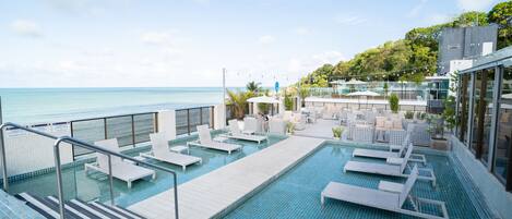 A pool area with lounge chairs and a view of the ocean.