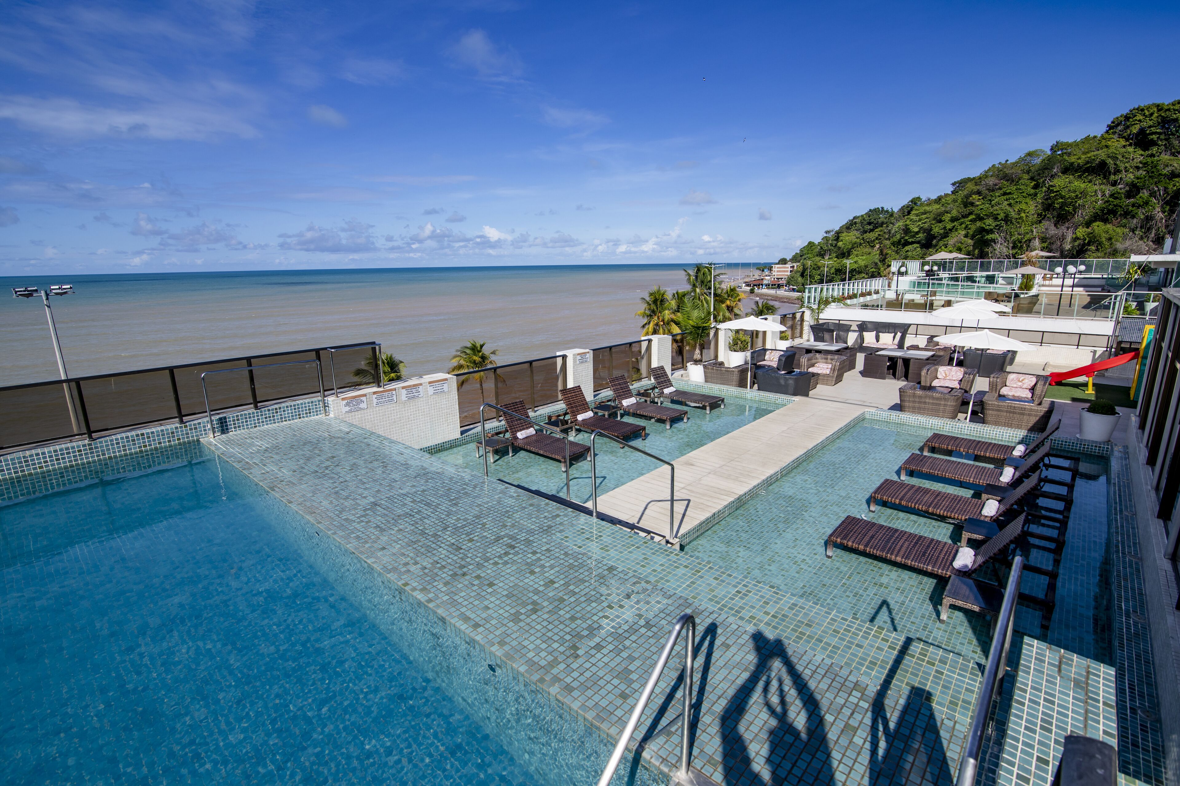 Piscina no terraço com espreguiçadeiras e vista para a praia.