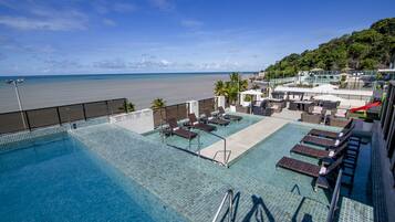 Piscina no terraço com espreguiçadeiras e vista para a praia.