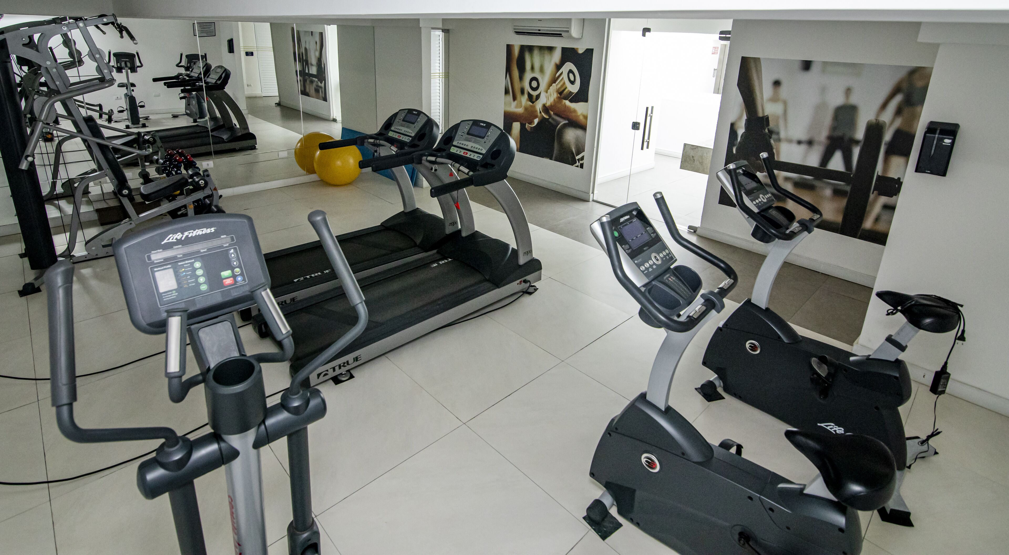 A gym with treadmills, elliptical machines, and exercise balls.