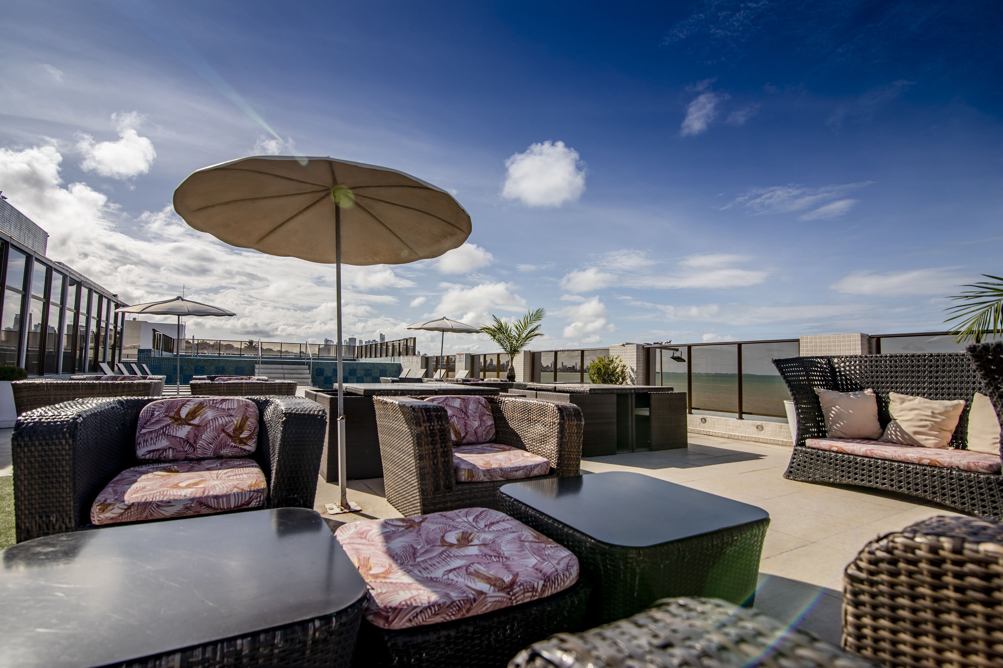 An outdoor seating area with wicker furniture and umbrellas, overlooking a body of water.
