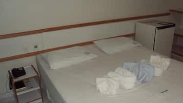 Habitación de hotel con una cama individual, una mesita de noche con lámpara, y una pequeña estantería con libros y un teléfono.