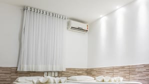 Ein Hotelzimmer mit zwei Betten, einem weißen Vorhang, einer Klimaanlage und einem gefliesten Boden.