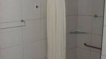 A small, enclosed shower area with a white shower curtain, a glass shelf, and a metal grab bar.
